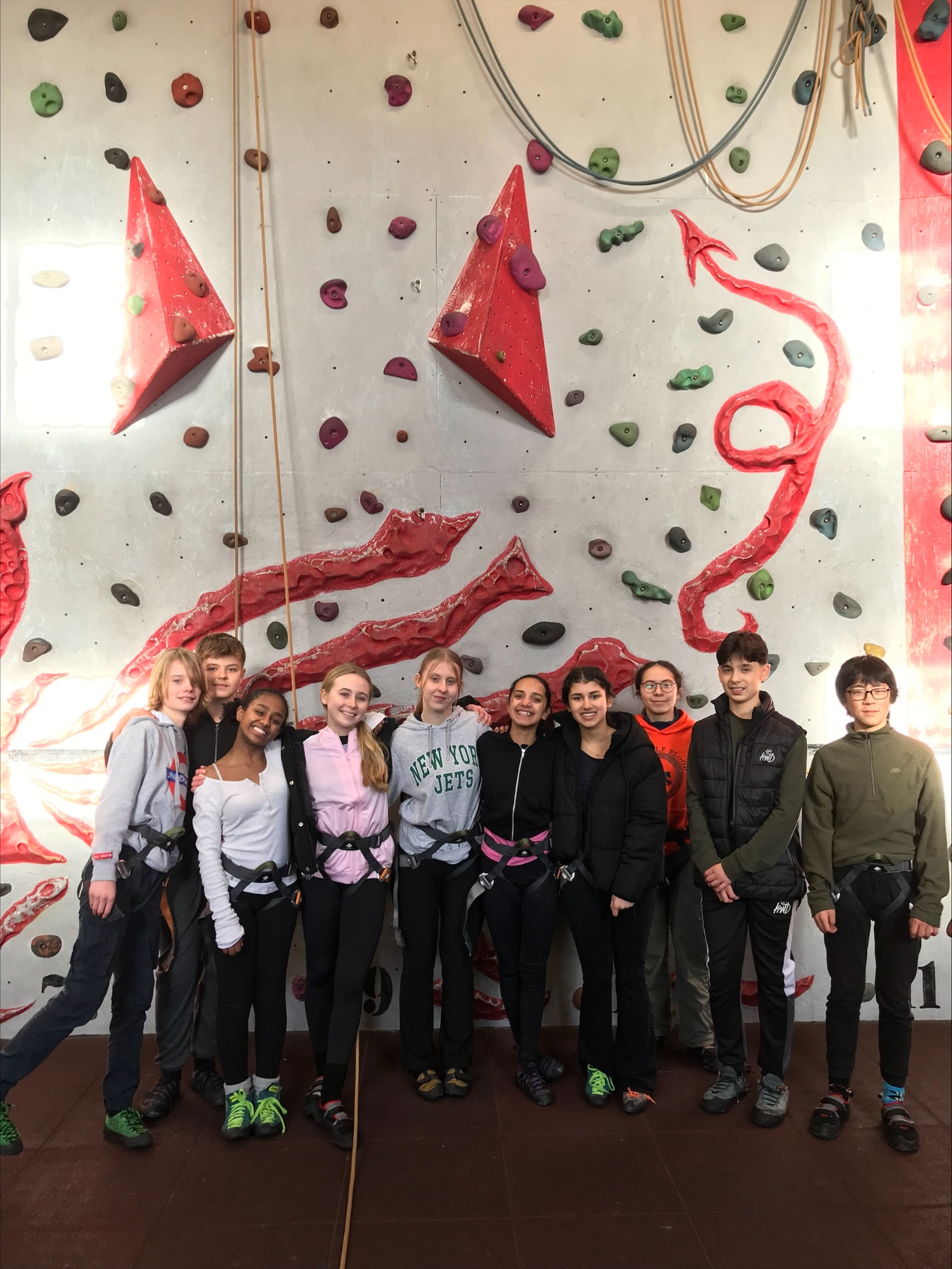 A group of students posing at the bottom of climbing wall