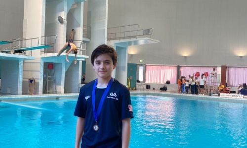 Josh posing in front of the swimming pool with his medal